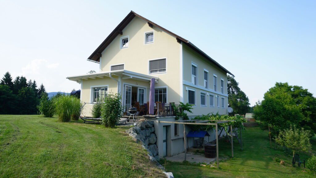 gelbes haus in hanglage mit neuem südseitigen zubau. baluer himmer und grüne wiesen rundherum.